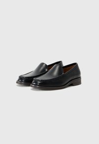Mocasines de cuero negro con textura suave, puntera redondeada y costuras decorativas en la parte frontal, con un tacón bajo apilado.