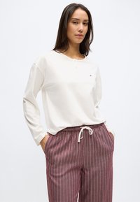 Balts garām piedurknēm top ar pogu sēriju un mazu logotipu, kopā ar burgundijas krāsas svītrainām biksēm ar auklu jostu un sānu kabatām.