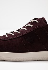 Burgundské semišové tenisky s bílými tkaničkami, texturovaný svršek, kontrastní gumová podešev a nenápadný logový detail na boku.