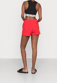 Shorts de sport rouges avec une taille élastique, poche arrière, associés à un débardeur noir ajusté et des sandales slides noires.