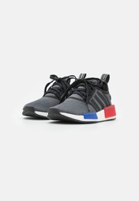 Black athletic shoes with gray mesh upper, three black stripes, a white midsole, and red and blue accents on the heel.