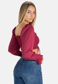 Bordeaux crop top med puffede ærmer og smockdetalje. Kombineres let med højtaljede denimjeans i en klassisk blå nuance.