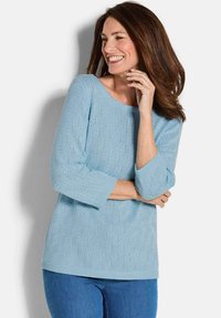 Helle blaue Strickjacke mit Dreiviertel ärmeln, strukturiertem Muster und gerippten Bündchen, kombiniert mit blauen Jeans.