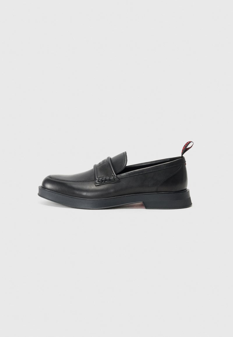 Sorte læder loafers med en glat finish, rund tå og dekorativ syning. Har en lav, chunky hæl og en rød løkke bagpå.