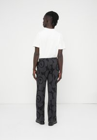 Μαύρο παντελόνι με αφηρημένο φλοράλ μοτίβο σε διάφορες αποχρώσεις του γκρι, συνδυασμένο με ένα απλό λευκό κοντομάνικο μπλουζάκι.