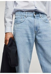 Los vaqueros de denim azul claro presentan un diseño clásico de cinco bolsillos con cremallera, un ligero desgaste y herrajes metálicos para el cierre.