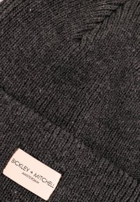 Grijze gebreide beanie met een ribbeltextuur, uitgerust met een crèmekleurig label met de tekst "BICKLEY + MITCHELL AMSTERDAM."