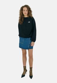 Sudadera negra con un logotipo blanco, combinada con una mini falda de mezclilla azul. El calzado incluye tacones negros de punta y calcetines de estampado de leopardo.
