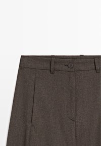 Pantaloni marroni, testurizzati, con vestibilità dritta, pieghe e chiusura con bottone. La vita ha passanti per la cintura; il tessuto presenta un motivo tessuto.
