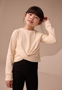 Haut à manches longues côtelé crème avec un détail noué à l'avant, assorti à un pantalon ajusté côtelé noir. Tissu doux avec une texture lisse.