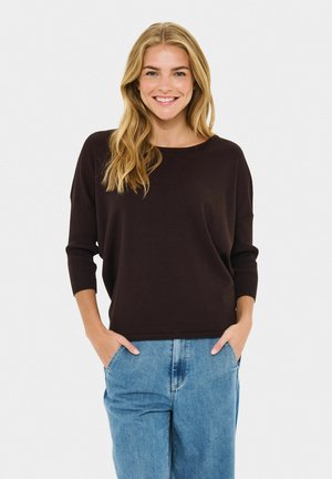 Dunkelbrauner, locker sitzender Pullover mit gerippten Ärmeln, kombiniert mit hellblauen, locker sitzenden Jeans. Schlichtes Design mit rundem Ausschnitt.