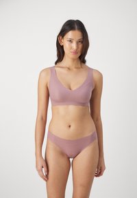 Lyse rosa sømløs bralette og matchende truser laget av myk, elastisk stoff med en glatt tekstur. Begge har et enkelt design og ingen hardware.