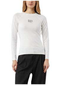 Biała koszula z długim rękawem, z okrągłym dekoltem i raglanowymi rękawami. Na środku czarny nadruk tekstowy. Tkanina wygląda na gładką i dopasowaną.