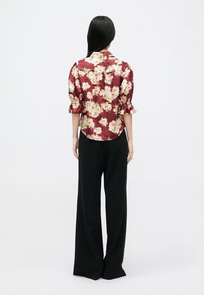 Virágmintás bordó blúz puffos ujjakkal és kerek hem kiképzéssel, laza fekete nadrággal párosítva. Simább, fényes anyagtextúra.