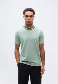 Ανοιχτό πράσινο κοντομάνικο T-shirt με μαύρο ριμπ ύφασμα στο γιακά και λογότυπο "BOSS". Μαλακό ύφασμα, casual εφαρμογή. Φορεμένο με σκούρο cargo παντελόνι.