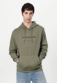 Alyvuogių žalios spalvos džemperis su priekine kišenėle, virvute reguliuojama kapuca ir juodai raudonu „TOMMY HILFIGER“ logotipu. Minkšta medžiaga su surišamomis rankovėmis.