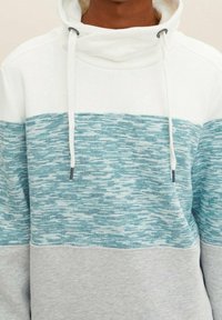 Felpa con cappuccio con una parte superiore bianca e un motivo testurizzato blu-verde, caratterizzata da un fondo grigio, cordini e rifiniture con tasche frontali.