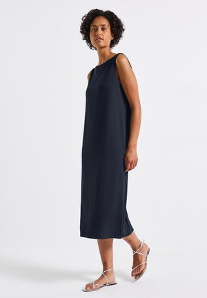 Navy ribbed sleeveless dress with a straight cut and side slits, complemented by silver strappy sandals. Smooth texture and simple design.