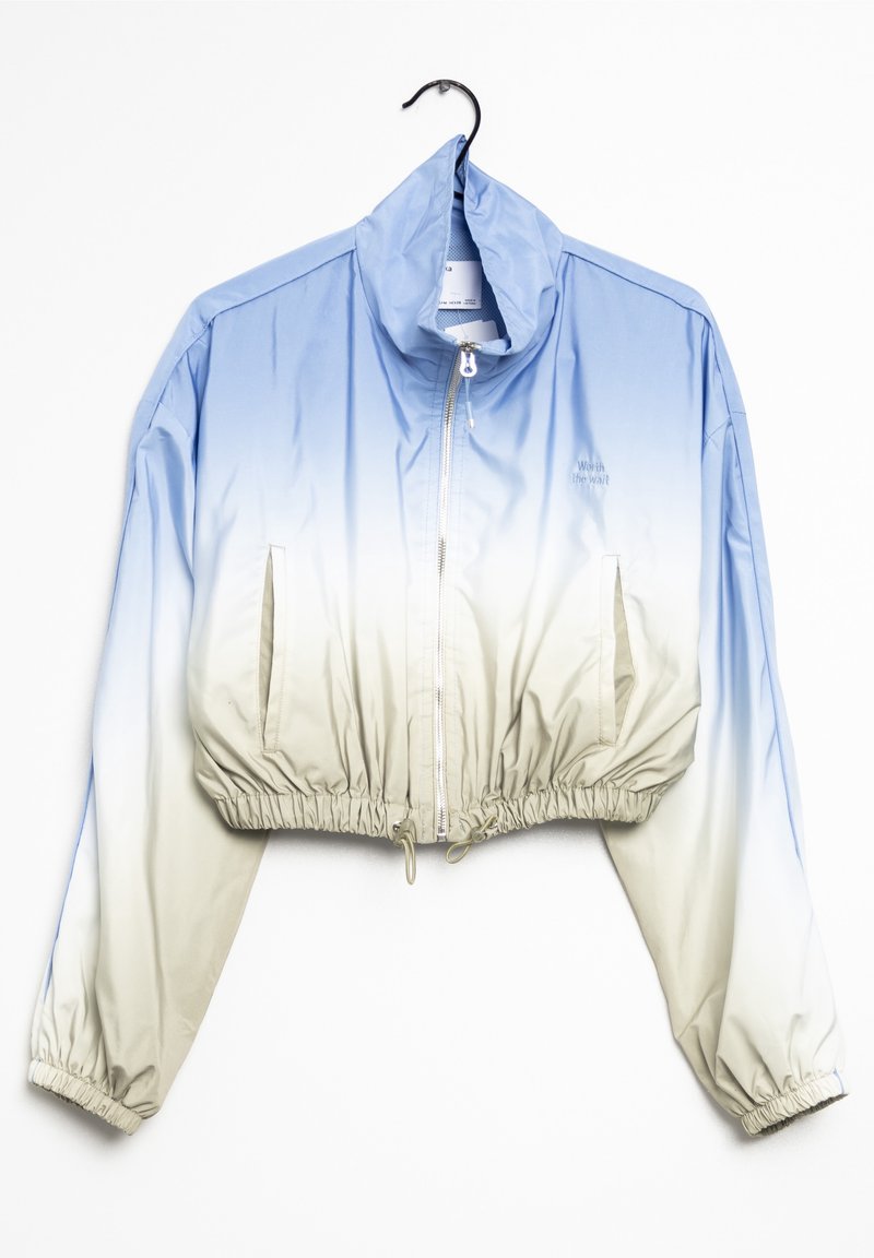 Cropped windbreaker jacket in blue gradient, shifting to light beige. Features elastic cuffs, adjustable drawstring hem, and side pockets.