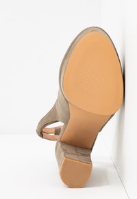 Sandale à talon fermée en daim taupe, présentée en angle pour montrer la semelle texturée beige et le petit talon carré sur une surface blanche.