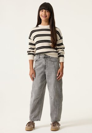 Pull en maille rayé crème et noir, associé à un jean large délavé gris. Des baskets marron à lacets complètent cette tenue décontractée.