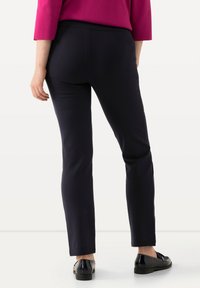 Pantalones azul marino ajustados con cintura elástica, combinados con zapatos de charol negros. El fondo es neutral, resaltando el conjunto.