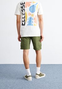 Un t-shirt blanc à manches courtes avec des graphismes colorés ; un short cargo vert olive ; des chaussettes blanches ; des baskets vertes et crème.