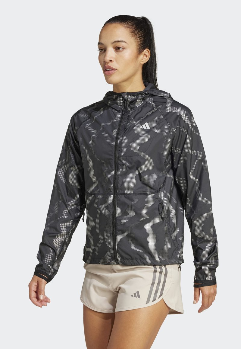 Letvægts sort jakke med et geometrisk gråt mønster. Har hætte, frontlynlås og justerbare manchetter. Sat sammen med lette shorts.