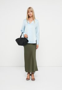 Svijetloplava bluzica dugih rukava s ovratnikom; maslinasto zelena lepršava maxi suknja; crna torbica; crno-bijele sandale na visoku petu s remenčićima.