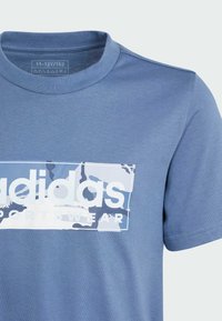 Camiseta de algodón azul con un logo de estampado de camuflaje. Cuello redondo, mangas cortas, con una textura suave y hombros sin costuras.