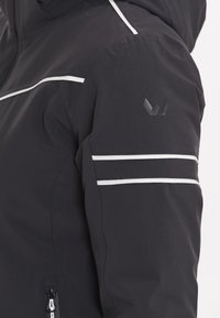 Svart jacka med vit kant längs axlarna och ärmarna, med en glänsande svart logotyp på överarmen. Syntetiskt material, slät textur.