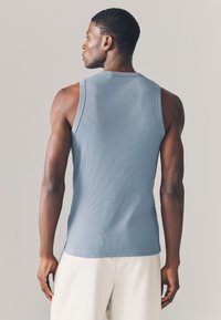 Top a costine azzurro chiaro con ampie aperture per le braccia e orlo diritto, abbinato a pantaloni color crema. Texture liscia che migliora il comfort.