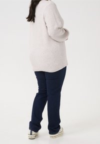 Lys grå strikket sweater med en afslappet pasform, der har glitrende detaljer. Parret med mørkeblå denim jeans og hvide sneakers.