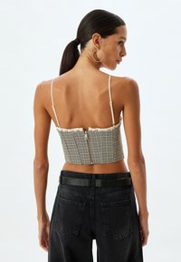 Afskåret, ternet top med justerbare spaghetti stropper, blondekant ved halsudskæringen og lynlås lukning bagpå, parret med højtaljede sorte jeans.