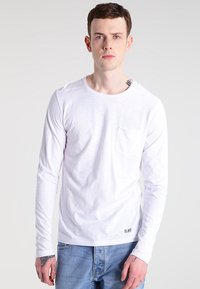 Langärmliges weißes T-Shirt mit Rundhalsausschnitt, Tasche auf der linken Brust, strukturiertem Stoff und Markenlogo am unteren Saum.