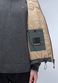 Grauer Pullover mit geripptem Saum und Norwegen-Flaggen-Detail, unter einer beigen Steppjacke mit einer grünen Tasche und Logo-Patch getragen.