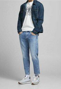 Jeansjacka i mörkblå färg, vit t-shirt med grafiskt tryck, ljusblå jeans och vita sneakers med grå detaljer.