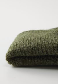 Folded olive green knitted fabric with visible ribbing pattern on a plain white surface.