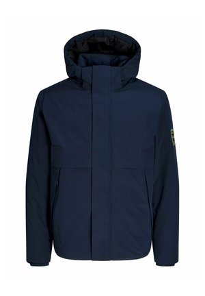 Chaqueta impermeable de color azul marino con cuello alto, cierre frontal y grandes bolsillos en el pecho. Cuenta con un parche de logo en la manga izquierda.