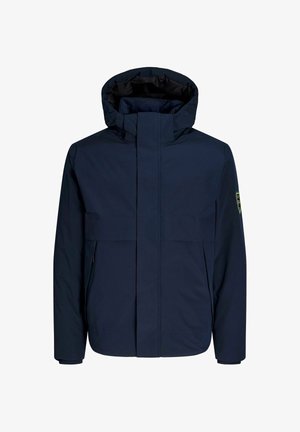 Navy blue waterproof jacket with a high collar, front zip, and large chest pockets. Features a logo patch on the left sleeve.