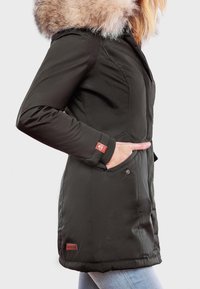 Sort parka-jakke med faux fur hætte. Har sidelommer, ribbede manchetter og et logo patch. Glat, blødt materiale med en tætsiddende design.