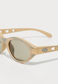 Ochelari de soare bej cu o textură unică asemănătoare lemnului, lentile rotunde și un accent metalic subtil pe brate. Design ușor.