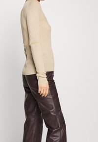 Pull à manches longues côtelé beige clair, avec une coupe près du corps et une texture douce, porté avec un pantalon en cuir marron foncé.