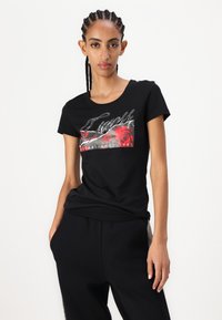 Black cotton t-shirt featuring a floral graphic with red roses, sparkling text, and a round neckline. Paired with black pants.