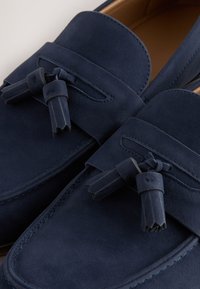 Mocassins en daim bleu marine avec détails à pampilles et bouts carrés arrondis, dotés d’une doublure en cuir souple et de coutures le long des bords.