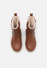 Brązowe skórzane botki za kostkę z teksturowanym wykończeniem, sztucznym futerkiem wewnątrz i bocznymi zamkami. Okrągły czubek i gumowa podeszwa zapewniająca stabilność.