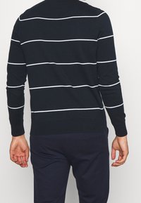 Pull en maille bleu marine avec des rayures horizontales blanches, col rond, poignets et ourlet côtelés. La vue de dos met en valeur le design à rayures.