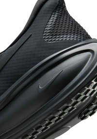 Chaussure de sport noire avec une tige texturée et une semelle intermédiaire lisse, arborant un logo Nike Swoosh visible et une semelle extérieure à motif pour une meilleure adhérence.