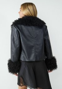 Czarna kurtka z sztucznej skóry w kroju cropped z puszystym czarnym kołnierzem i mankietami. Kurtka charakteryzuje się gładką fakturą i dopasowanym kształtem.