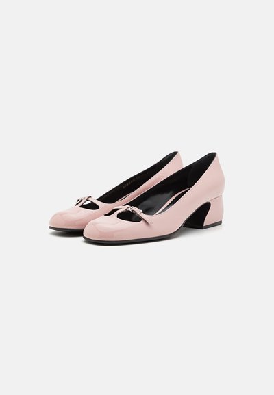Scarpe con tacco alto in pelle sintetica rosa, con punta arrotondata, design a ritaglio e un piccolo fiocco decorativo nella parte anteriore. Tacco spesso.